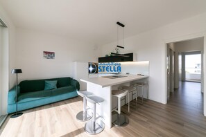 A modern apartment with a kitchen island, bar stools, a green sofa, and a minimalist design. - residence Adele # swimming pool + modern # (Jesolo)