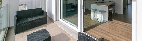 Un balcone moderno con mobili in rattan, una porta scorrevole in vetro che dà su una zona cucina con sgabelli da bar.