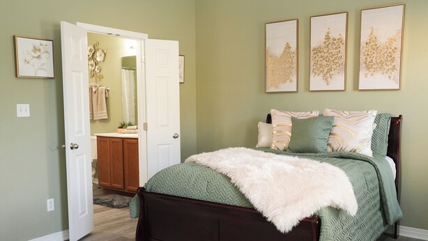 Ein Schlafzimmer mit einem Bett, einer Tür zu einem Badezimmer und drei gerahmten Kunstwerken an der Wand.