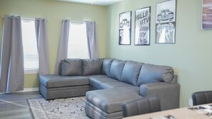 Ein Wohnzimmer mit einem Ecksofa, einem Deckenventilator und gerahmten Automobilposter an der Wand.