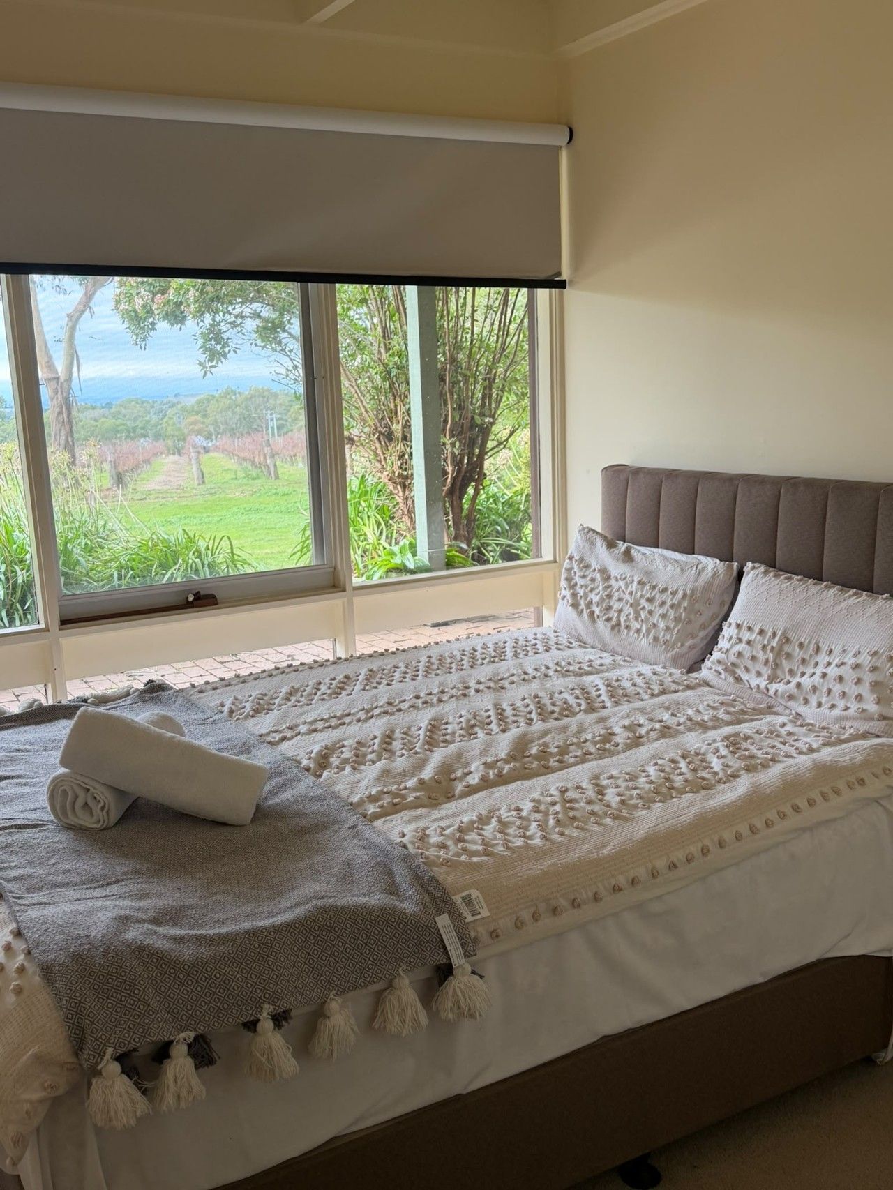 Una cama con una colcha y almohadas estampadas, un ventanal con vistas a la vegetación y un techo con una lámpara.