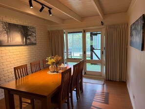 A dining area with a wooden table and chairs, a vase with flowers, and a painting on the wall.