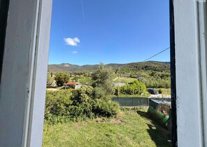 Blick durch ein Fenster auf eine ländliche Landschaft mit Hügeln, Vegetation und einigen Gebäuden.