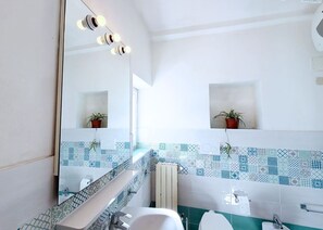 Ein modernes Badezimmer mit großem Spiegel, zwei Zimmerpflanzen, einer gefliesten Rückwand und einer Toilette.