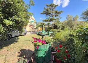 Ein Garten mit einem Brunnen, Topfpflanzen und einem Auto im Hintergrund.