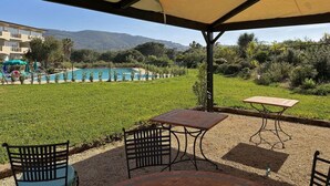 An outdoor patio with a table and chairs, a pool, and a view of a building and hills in the background. - Residenza Verde Blu - Verde Blu Primo Piano (620) (Capoliveri)