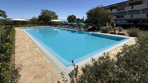 A rectangular swimming pool with a stone deck, surrounded by lounge chairs and umbrellas, with a building in the background. - Residenza Verde Blu - Verde Blu Primo Piano (620) (Capoliveri)