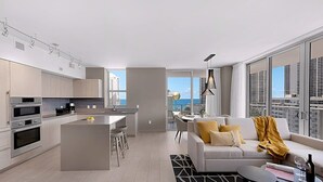 En modern lägenhet med kök, matplats och vardagsrum. Den har ett stort fönster med utsikt över staden, en soffa med kuddar och ett litet bord med en vinflaska.