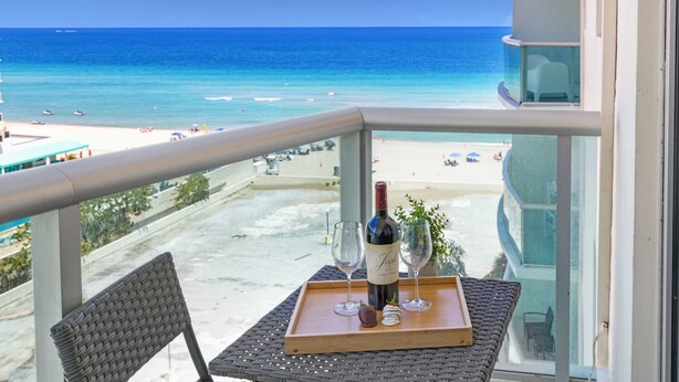 En balkon med udsigt over stranden, en vinflaske og et fad med glas og jordbær.