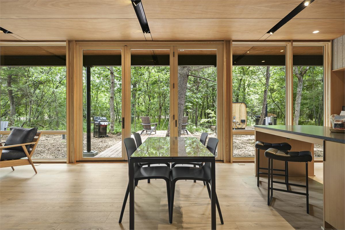 Eine moderne Küche mit einer großen Kochinsel, Holzboden und großen Fenstern mit Blick auf den Wald.