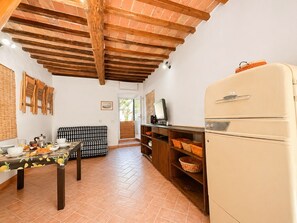 A kitchen with a tiled floor, a wooden ceiling, a refrigerator, a dining table with chairs, and a patterned sofa. - Bilocale Barbarossa a Porto Azzurro (Porto Azzurro)