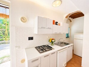 A kitchen with white cabinets, a gas stove, a sink, and a clock on the wall. - Bilocale Barbarossa a Porto Azzurro (Porto Azzurro)