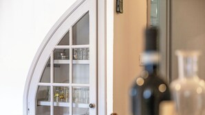 Une pièce avec une porte blanche en arc de cercle, un meuble vitré contenant des ustensiles de cuisine et une bouteille posée sur la table.
