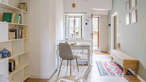 Un couloir comprenant un bureau, une chaise, une bibliothèque, un banc en osier et un tapis à motifs.