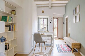 Ein Flur mit Schreibtisch, Stuhl, Bücherregal, Rattanbank und einem gemusterten Teppich.