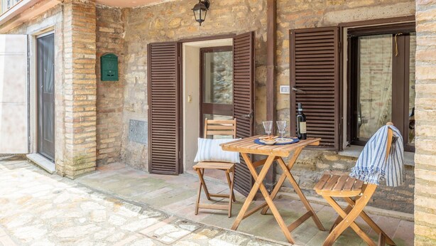 Un bâtiment en pierre avec des volets en bois, une table avec des chaises et une bouteille de vin posée sur la table.
