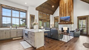 A spacious kitchen with large windows, a stone fireplace, and a high wooden ceiling. - Luxury 4BR Retreat in Eagle's Nest | Hot Tub, 2 Fireplaces & Mountain Views (Banner Elk)