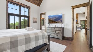 A bedroom with a large bed, a dresser, a painting, and a view of mountains through a window. - Luxury 4BR Retreat in Eagle's Nest | Hot Tub, 2 Fireplaces & Mountain Views (Banner Elk)