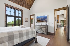 Ein Schlafzimmer mit einem großen Bett, einem Schminktisch, einem Gemälde und Bergblick durch ein Fenster.
