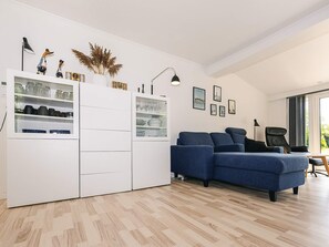 Una sala de estar moderna con un sofá seccional, un mueble blanco con puertas de vidrio y un ventanal que proporciona luz natural.