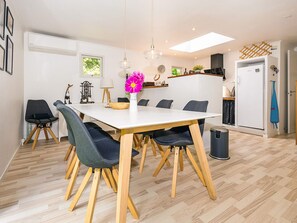 Un comedor moderno con una mesa blanca, sillas de madera y un florero con flores.