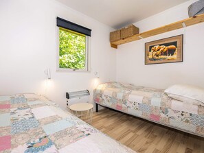 Un dormitorio con dos camas, una ventana con vistas a zonas verdes, un radiador, una mesita pequeña y un cuadro enmarcado en la pared.