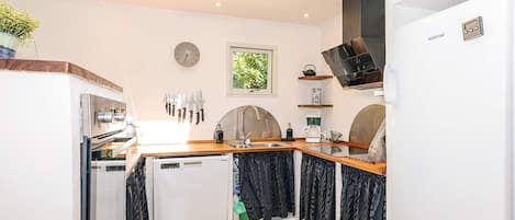 A compact kitchen with a dishwasher, a sink, and a stove. There is a clock on the wall and a window above the sink.