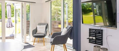 Een moderne woonkamer met een flatscreen televisie, twee grijze fauteuils, een salontafel en een lange bank.