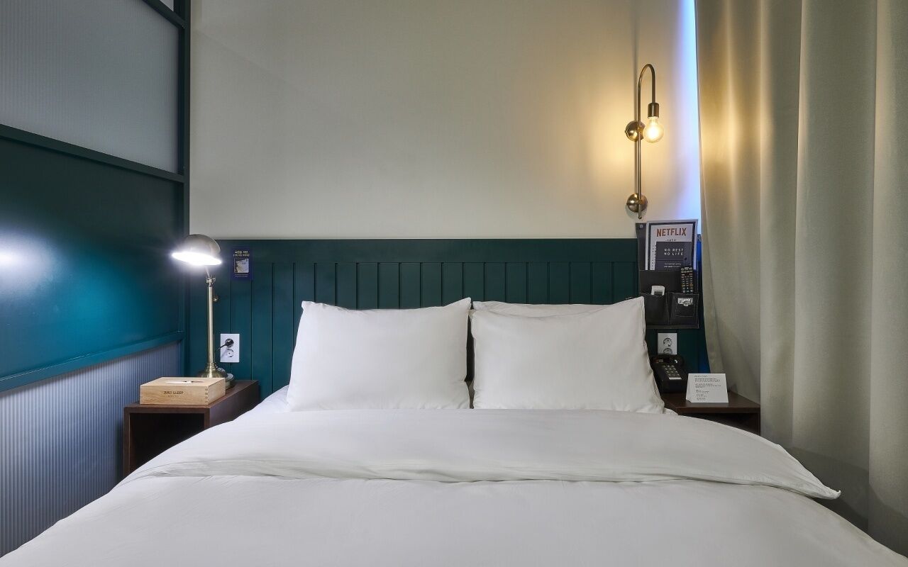A hotel room with a bed, a bedside lamp, a wall-mounted phone, and a Netflix sign.