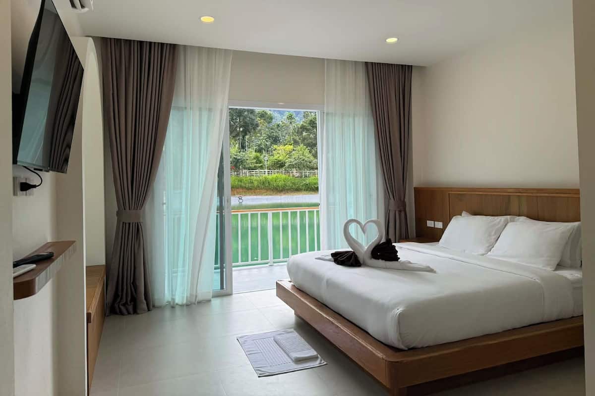 A hotel room with a bed, curtains, a TV, and a view of greenery outside.