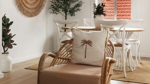 Ein Zimmer mit einem Korbstuhl, einem weißen Tisch mit einer dekorativen Platte, einer gewebten Wanddekoration und einer Topfpflanze.