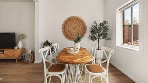 Ein Essbereich mit einem runden Holztisch, weißen Stühlen, einem gewebten Wandbehang und einem Blumentopf.