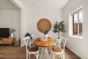 Ein Essbereich mit einem runden Holztisch, weißen Stühlen, einem gewebten Wandbehang und einem Blumentopf.