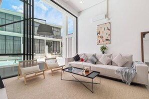 A modern living room with a sofa, coffee table, and chairs, large windows, and a balcony.