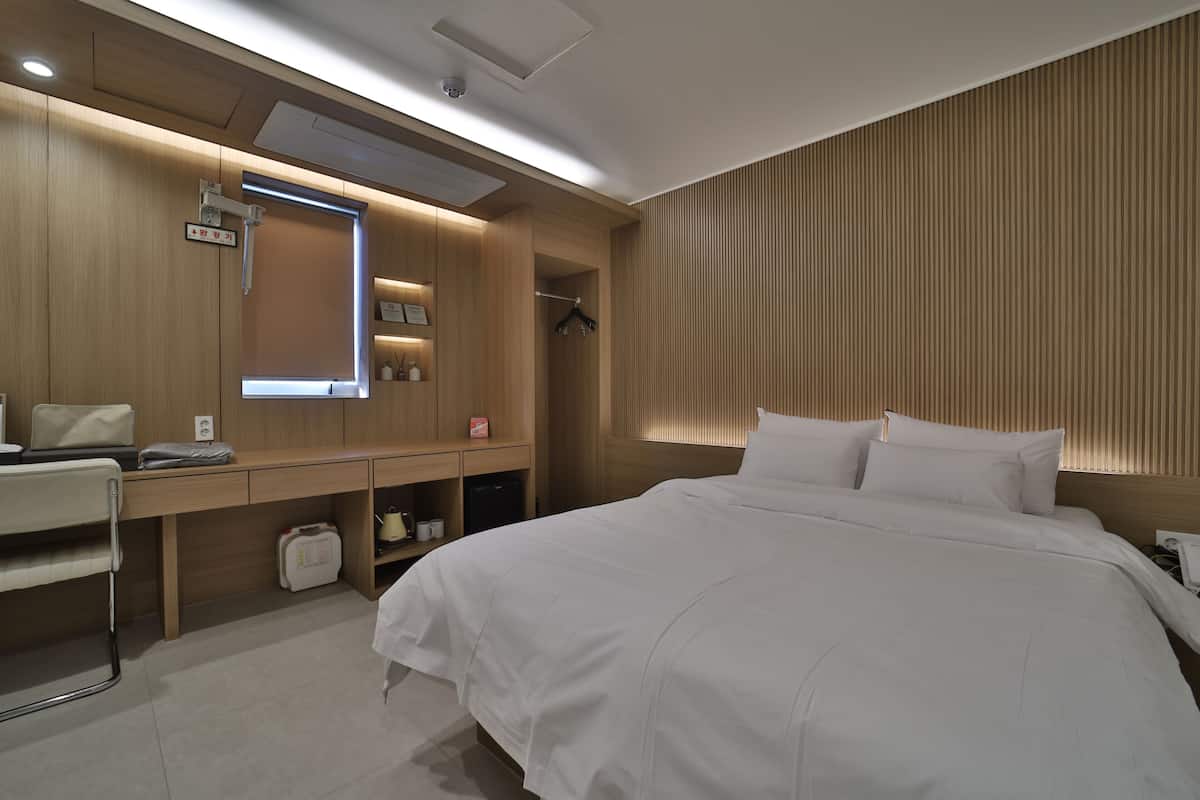 Habitación de hotel con cama, escritorio, espejo, armario y zona de ducha.