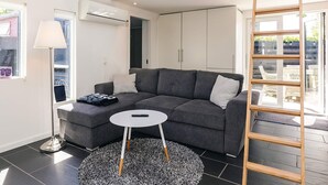 Ein modernes Wohnzimmer mit einem grauen Sofa, einem kleinen weißen Tisch, einer Stehlampe und einer Holzleiter.