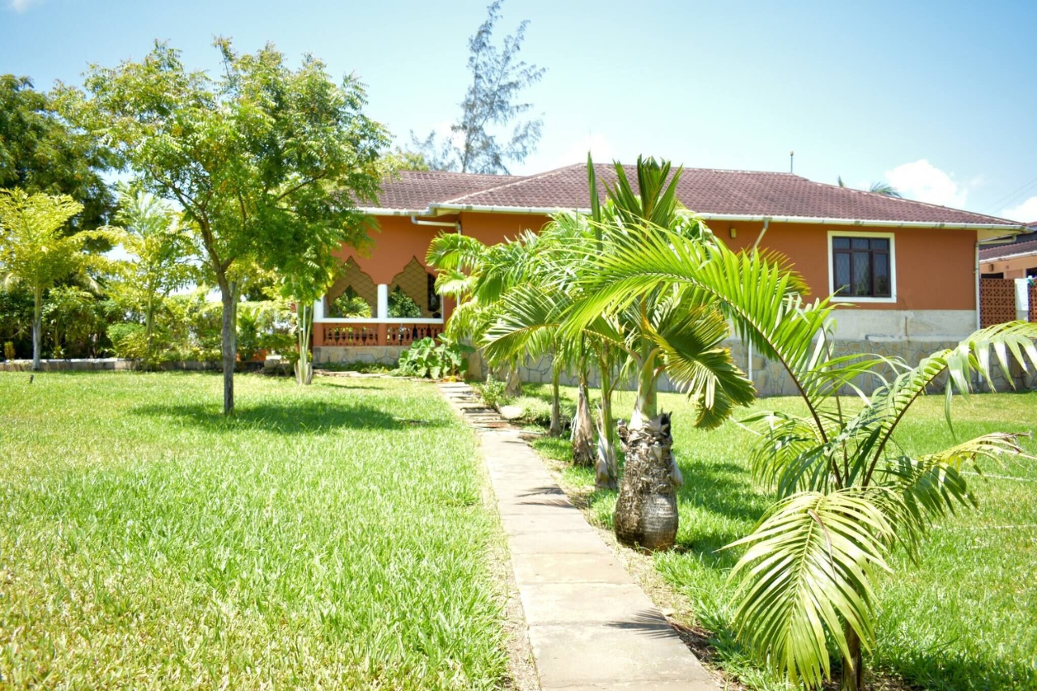 A residential house with a paved pathway, palm trees, and a well-maintained lawn.