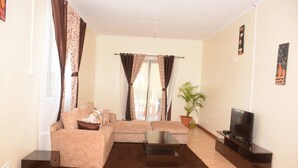 A living room with a sofa, a coffee table, a TV, and curtains. - Koriwo Gardens Kikambala Home Away From Home ! (Mtwapa)