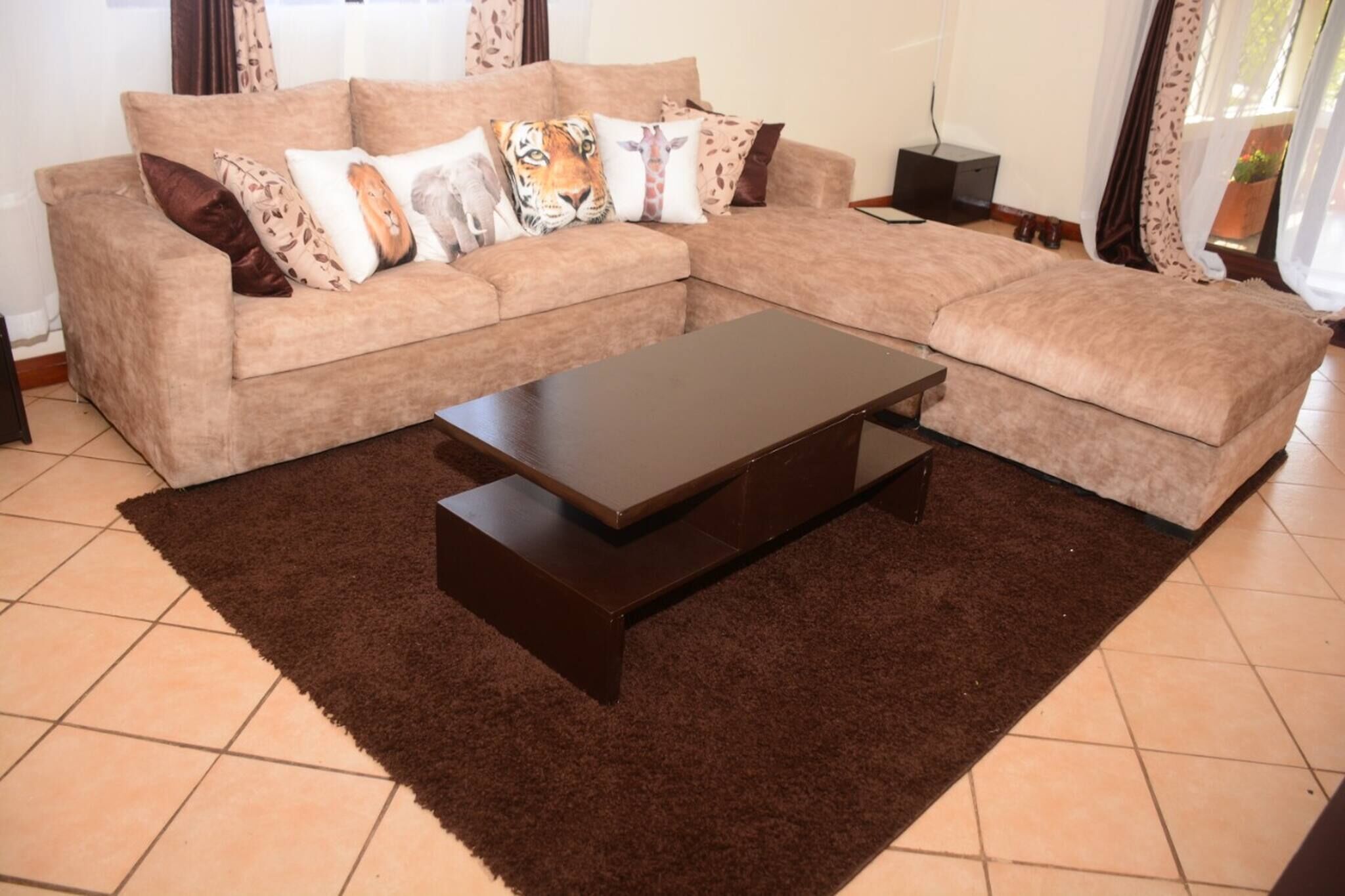 Een woonkamer met een hoekbank, een donker houten salontafel en een bruin vloerkleed.