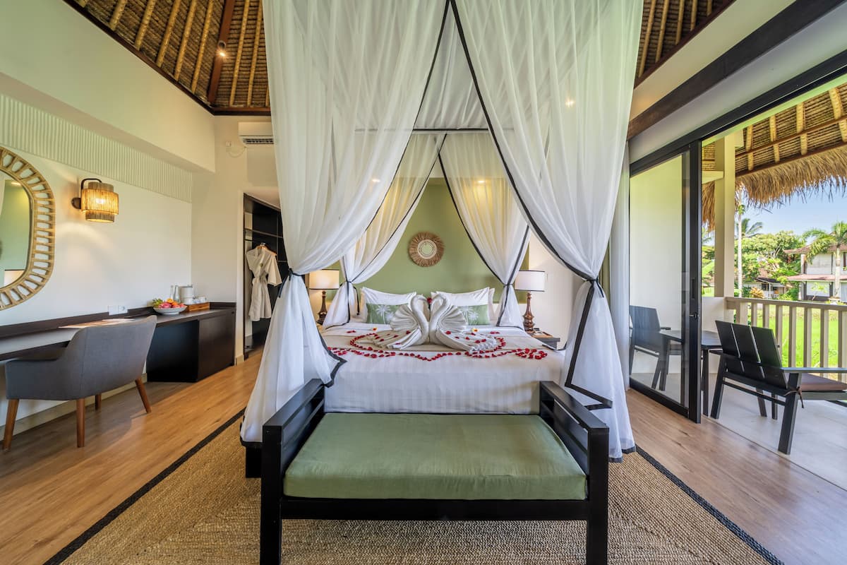 A bedroom with a canopy bed, a desk, a chair, and a view of the outdoors.