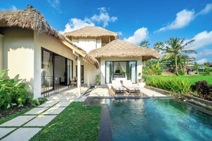 Un resort con piscina, edifici a tetto di paglia e vegetazione lussureggiante.