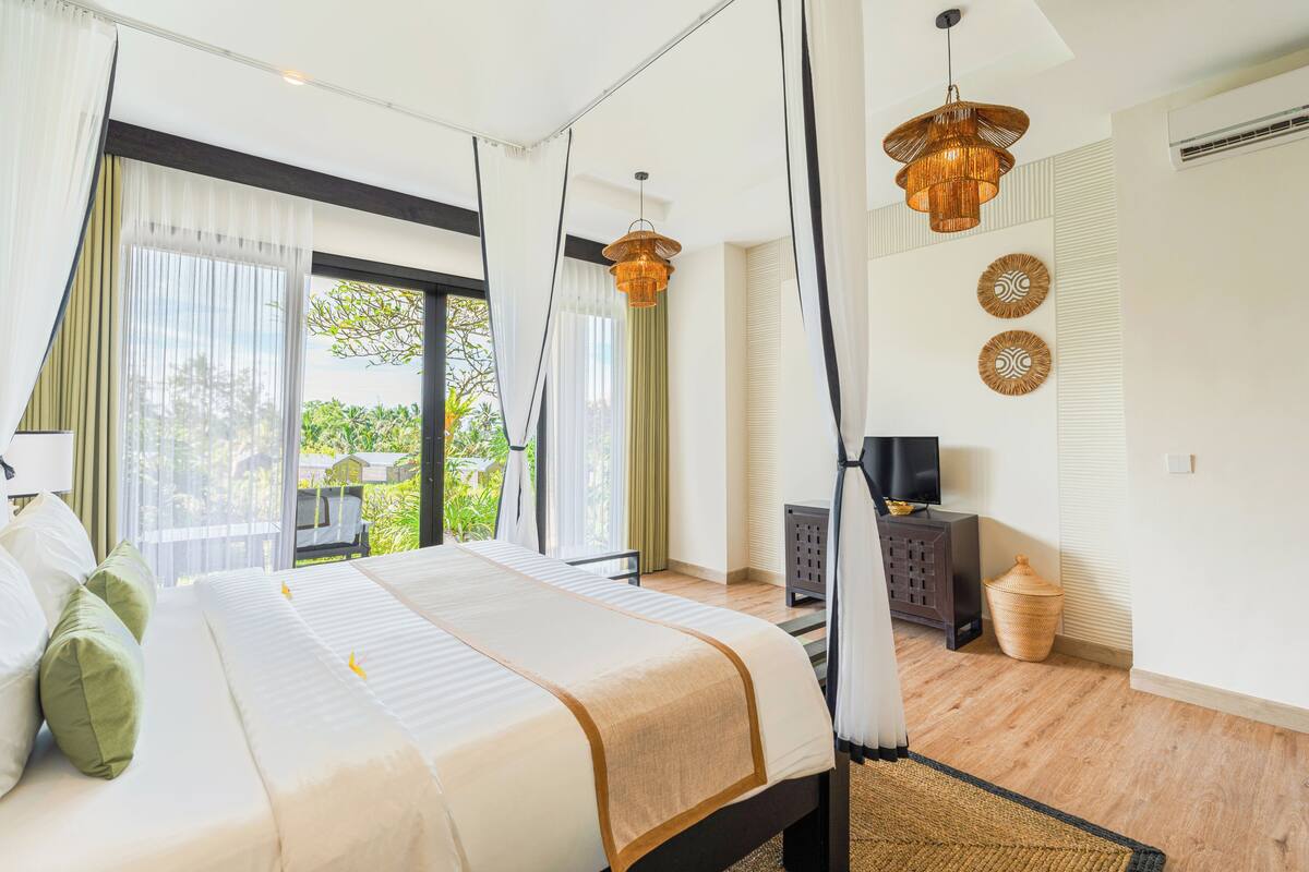 A modern hotel room with a large bed, a television, a wicker basket, and a view of greenery outside.