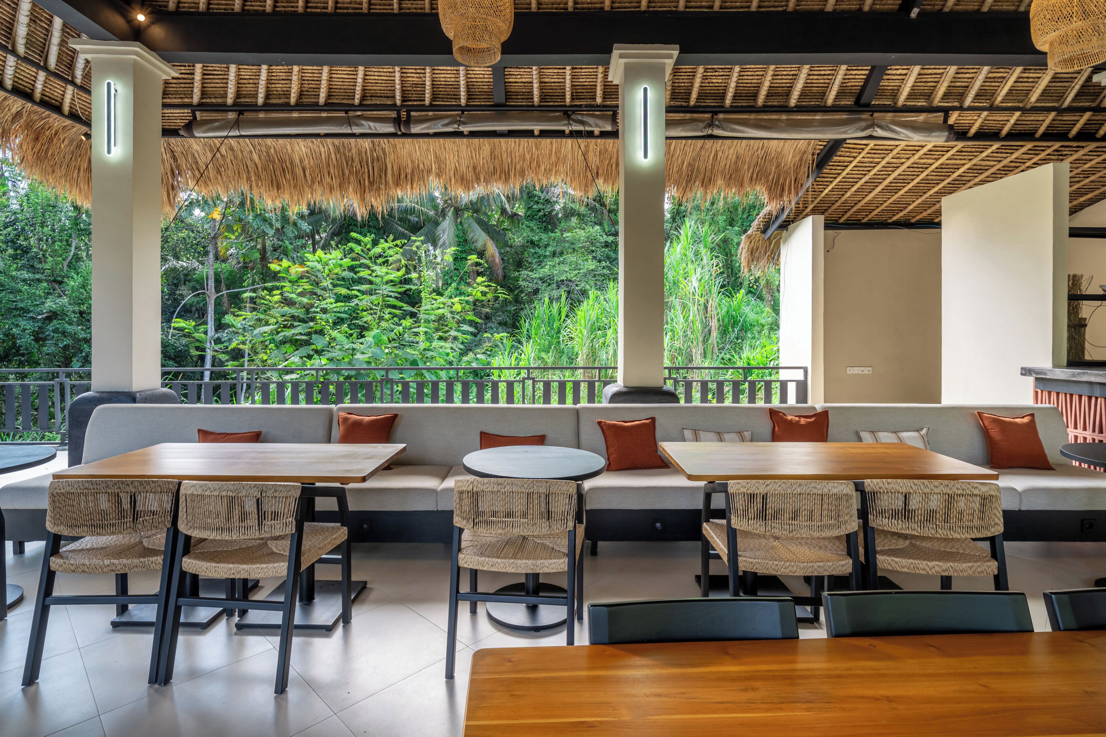 A modern outdoor seating area with thatched roof, cushioned benches, and wicker chairs.