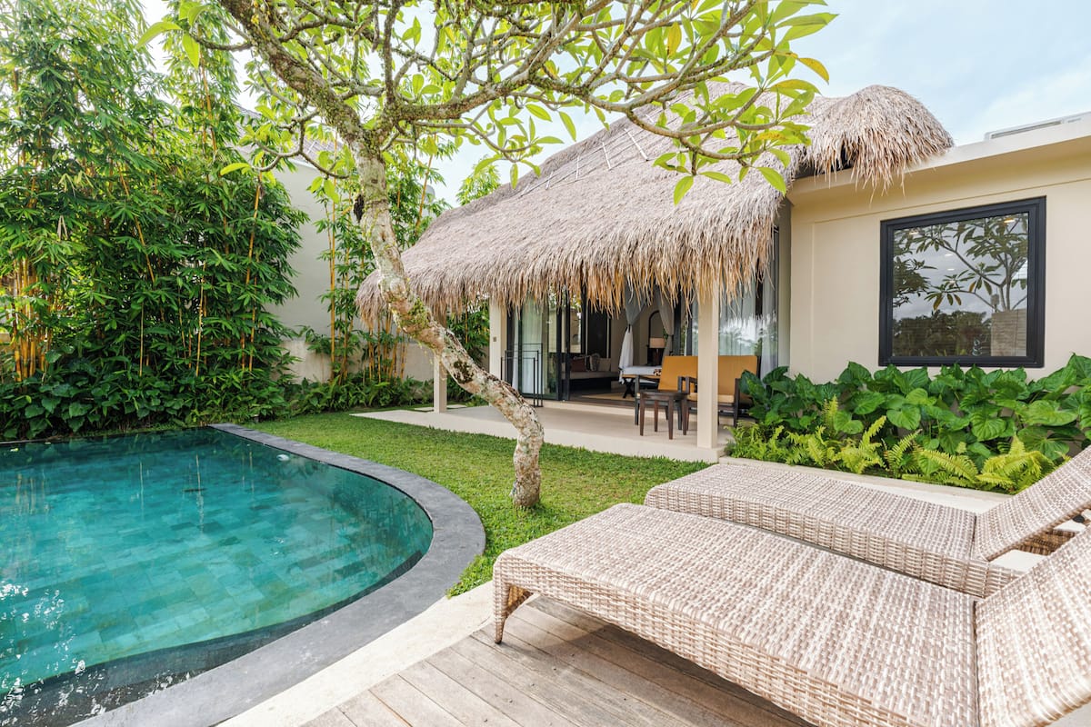 A poolside area with a thatched roof, lounge chairs, and a well-maintained garden.