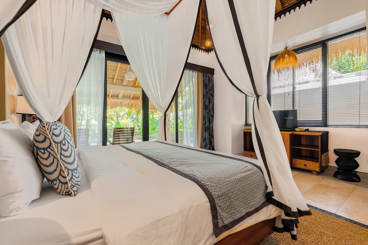 A bedroom with a four-poster bed, a television, and a window with blinds.