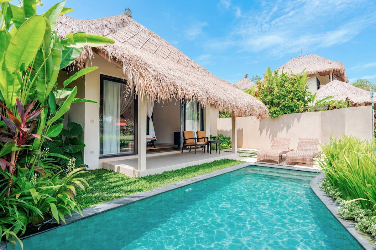 A poolside area with a thatched-roof structure, lounge chairs, and a clear blue pool.