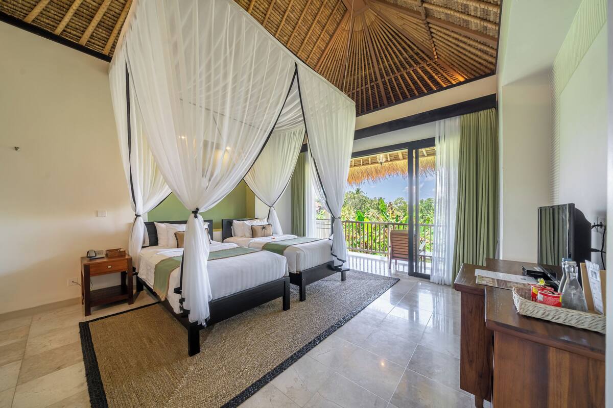 A bedroom with two beds, a balcony with a view, and a reception desk.