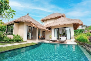 Un resort con piscina, construcciones de techo de paja y mobiliario exterior.