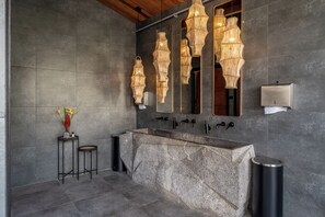 A modern bathroom with a granite sink, multiple mirrors, and a unique light fixture.