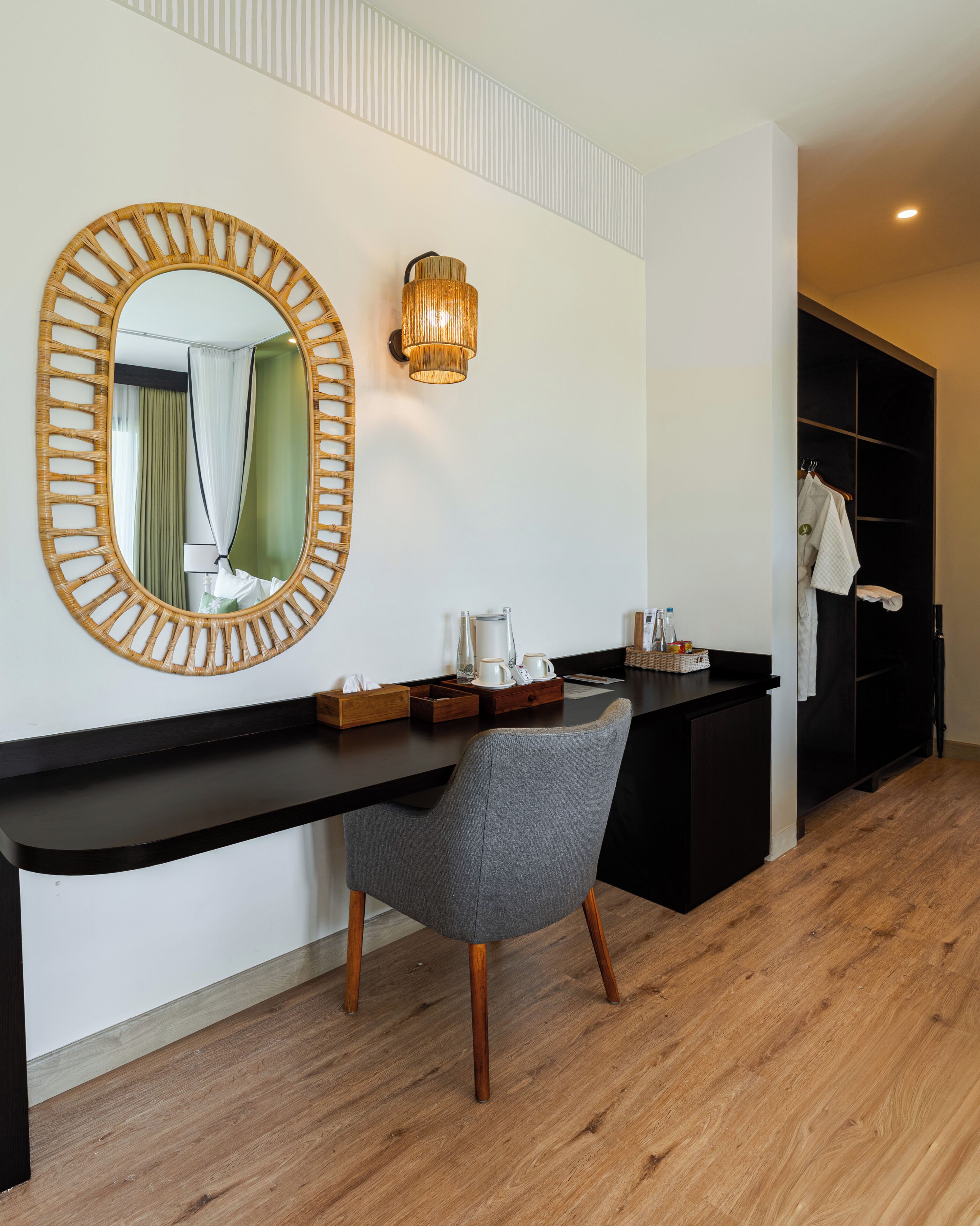 Ein modernes Hotelzimmer mit einem großen Spiegel, einer Wandleuchte, Holzboden, einem grauen Sessel und einem schwarzen Kleiderschrank.